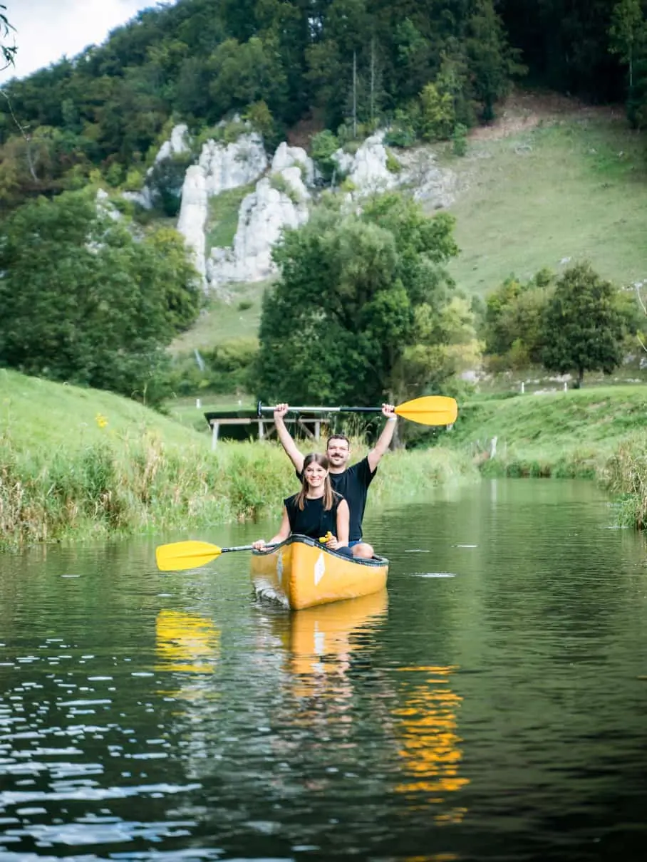 Alt: Steffi (sitzt vorne) und Gianni (sitzt hinten) in einem gelben Kanu auf der Lauter in Münsingen beim 21TORR Sommerfest 2023.
